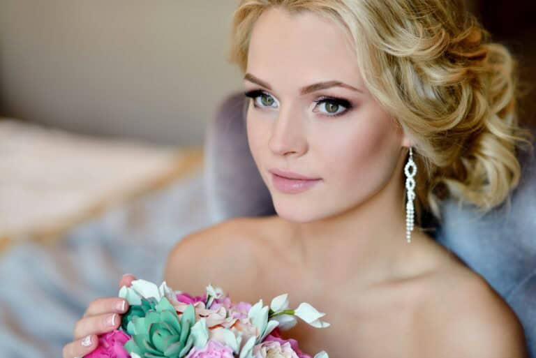 Beauty bride in bridal gown with bouquet and lace veil indoors